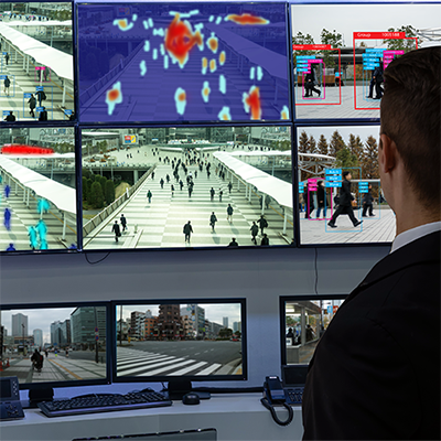 Person reviewing multiple security camera monitors, one in infrared.
